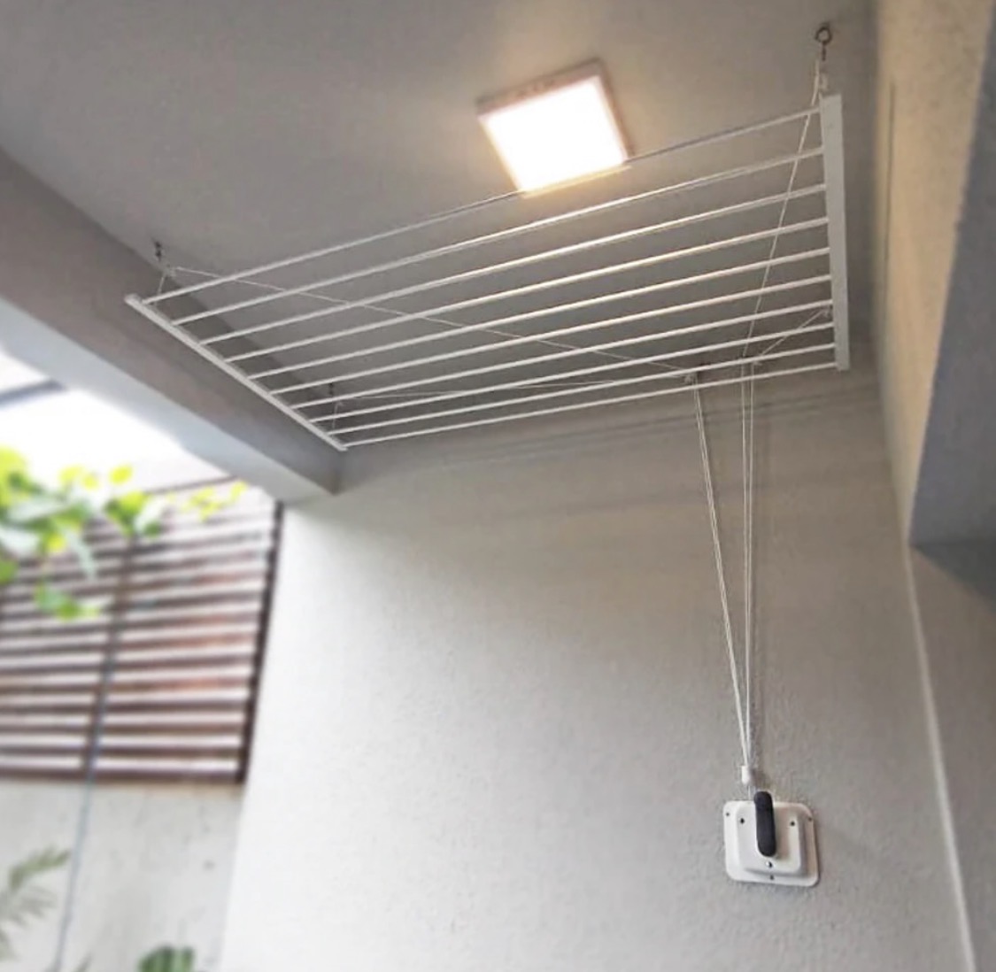 Varal de teto branco com manivela manual instalado em área de serviço